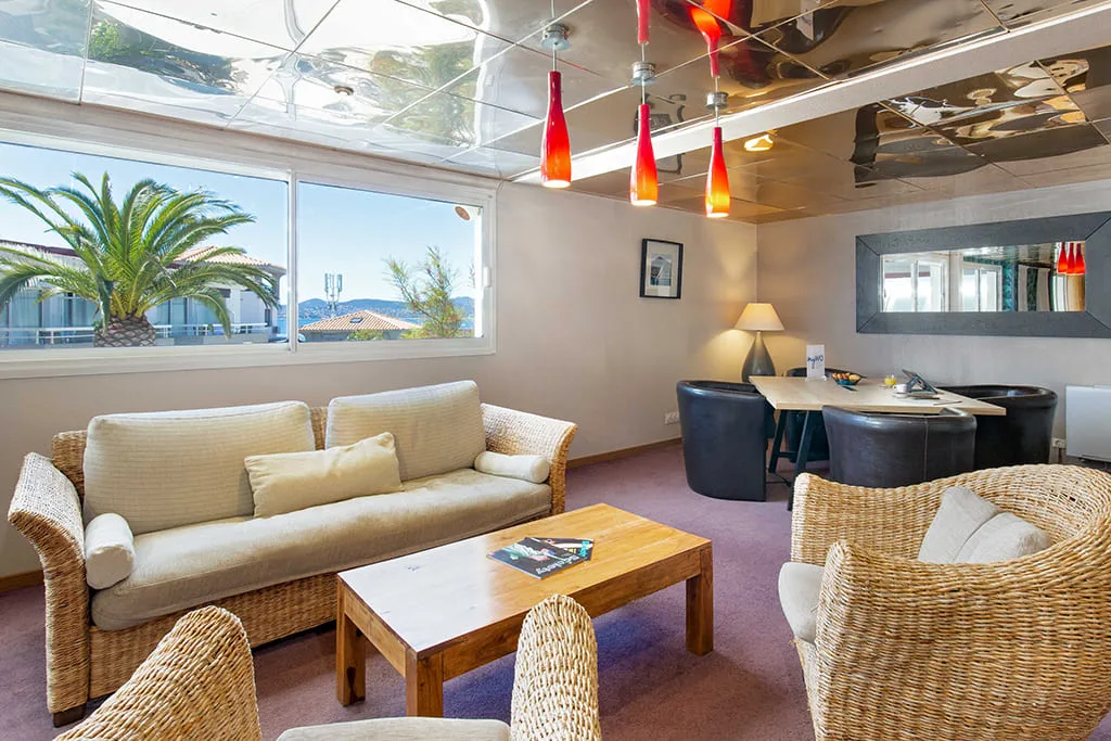 Salon lumineux avec canapés en osier et fenêtres.
