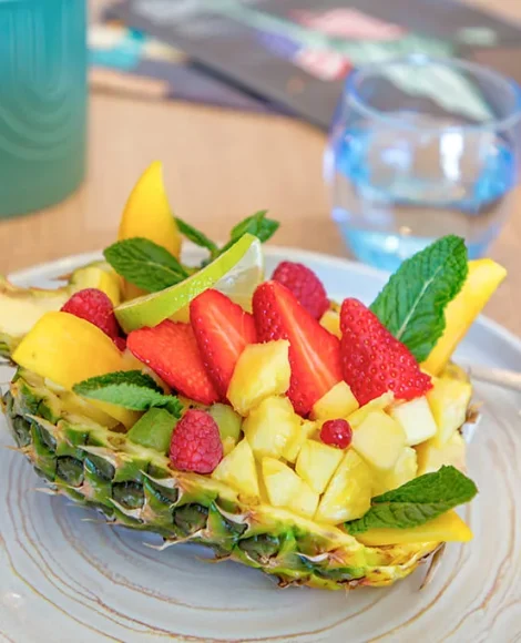 Salade de fruits dans demi-ananas sur assiette blanche.